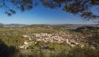 Vista panorámica de Mancor de la Vall con casas de piedra natural, rodeadas de colinas verdes y paisaje extenso.