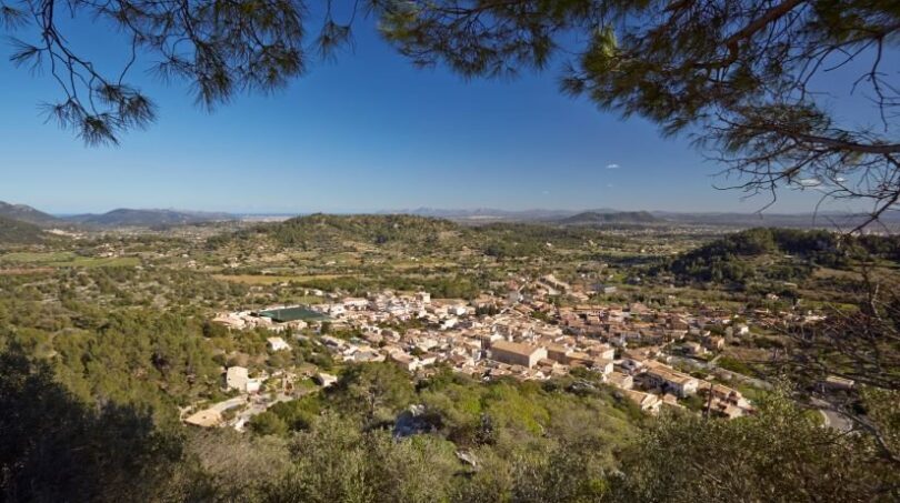 Vista panorámica de Mancor de la Vall con casas de piedra natural, rodeadas de colinas verdes y paisaje extenso.