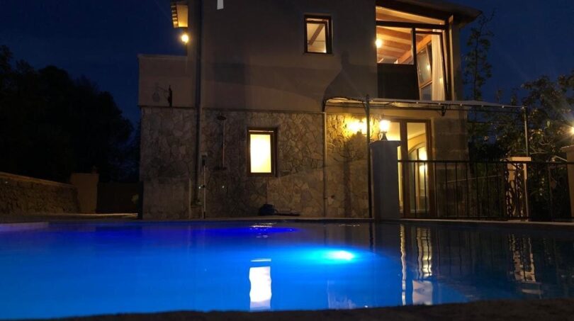 Finca Llucmajor: Beleuchteter Pool bei Nacht vor zweistöckigem Natursteinhaus mit warmem Lichtschein.