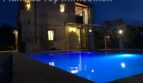 Beleuchteter Pool einer Finca in Llucmajor bei Nacht mit mediterranem Steinhaus im Hintergrund.