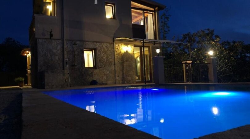 Beleuchteter Pool einer Finca in Llucmajor bei Nacht mit mediterranem Steinhaus im Hintergrund.