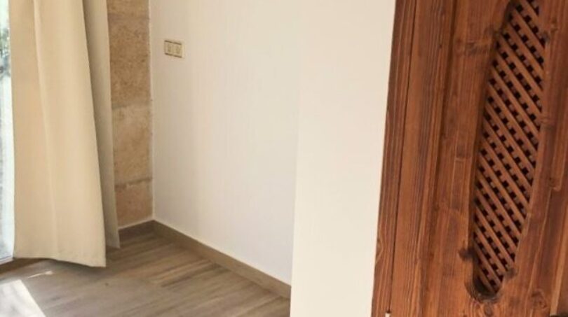 Heller Flur der Finca in Llucmajor mit Holzboden, rustikaler Holztür und Steinwand.