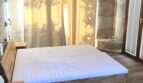 Schlafzimmer der Natur-Finca in Llucmajor mit Holzbett, Steinwänden und lichtdurchfluteten Vorhängen.