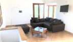 Helles Wohnzimmer der Finca in Llucmajor mit dunklem Ecksofa, Holzbalkendecke und Terrassentüren mit Naturblick.