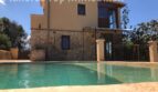 Finca Llucmajor: Außenansicht mit Pool, Natursteinwand und großzügiger Glasfront, eingebettet in mediterrane Landschaft.