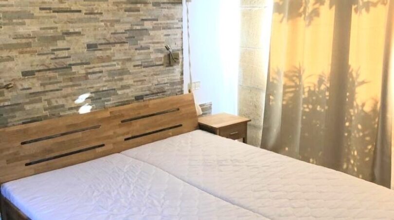 Schlafzimmer der Finca Llucmajor mit Doppelbett, Natursteinwand und Vorhängen mit Lichtspiel.