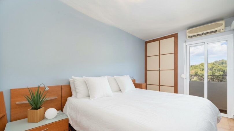 Helles Schlafzimmer mit Doppelbett, Holzmöbeln, Klimaanlage und Balkonzugang mit Naturblick