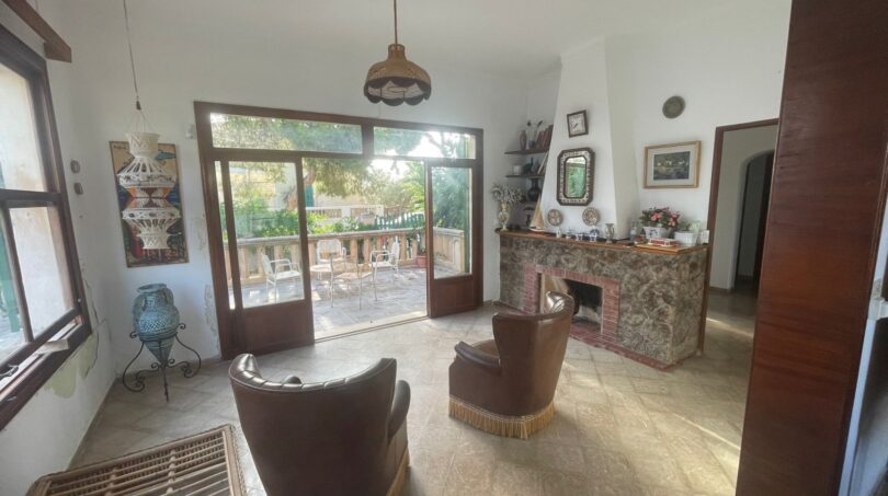 Wohnzimmer der mediterranen Villa mit Kamin, Ledersesseln und Terrassenzugang zum Garten in Porto Cristo.