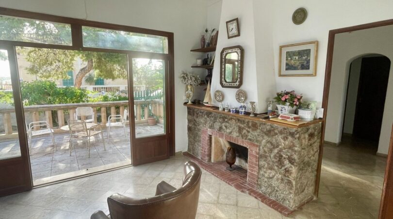 Wohnzimmer der mediterranen Villa in Porto Cristo mit Natursteinkamin, Lederstuhl und Terrassenzugang zum Garten.