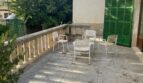 Geräumige Terrasse mit weißen Gartenstühlen, Steinbalustrade und grünen Fensterläden der mediterranen Villa in Porto Cristo.