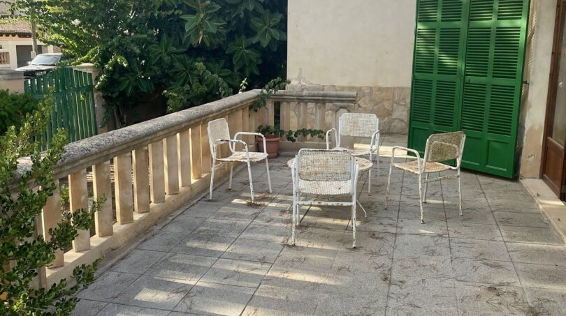 Geräumige Terrasse mit weißen Gartenstühlen, Steinbalustrade und grünen Fensterläden der mediterranen Villa in Porto Cristo.