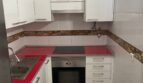 Moderne weiße Küche mit roter Arbeitsplatte, Einbauofen, Induktionskochfeld und Waschmaschine in Palma-Wohnung