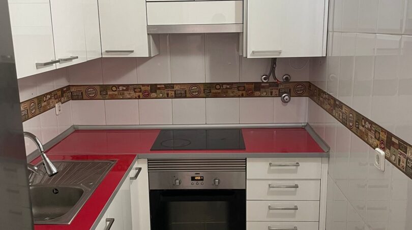 Moderne weiße Küche mit roter Arbeitsplatte, Einbauofen, Induktionskochfeld und Waschmaschine in Palma-Wohnung