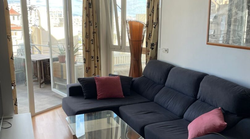 Helles Wohnzimmer mit dunkelblauem Ecksofa, Glasstisch und großen Fenstern mit Stadtblick über Palma