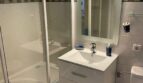 Helles Badezimmer mit Badewanne, Glasdusche, weißem Waschtisch und beleuchtetem Spiegel in Palma-Wohnung