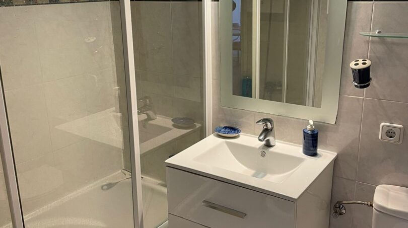 Helles Badezimmer mit Badewanne, Glasdusche, weißem Waschtisch und beleuchtetem Spiegel in Palma-Wohnung
