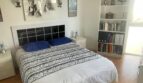 Helles Schlafzimmer mit Doppelbett, blauen Kissen, Bücherregal und Kunstwerken in Palma-Wohnung