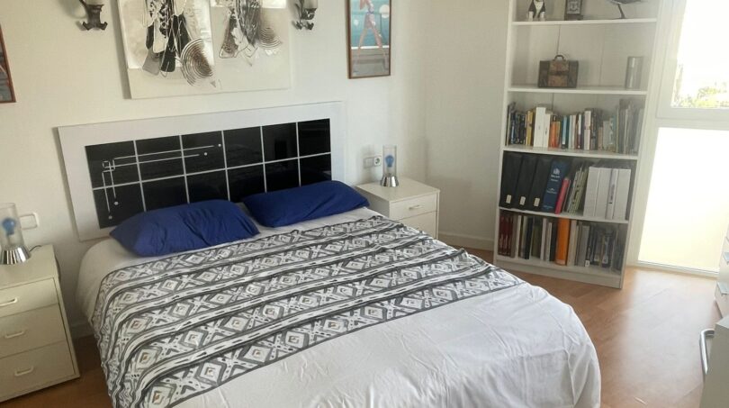 Helles Schlafzimmer mit Doppelbett, blauen Kissen, Bücherregal und Kunstwerken in Palma-Wohnung