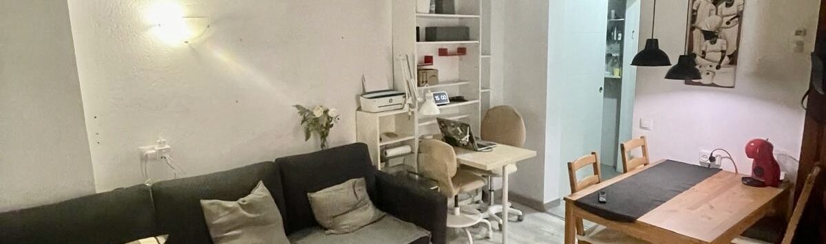 Sala de estar del apartamento del casco antiguo de Palma con techo de vigas de madera, sofá esquinero y mesa de comedor