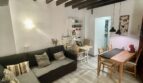 Sala de estar del apartamento del casco antiguo de Palma con techo de vigas de madera, sofá esquinero y mesa de comedor