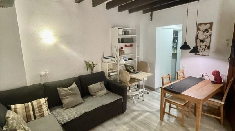 Sala de estar del apartamento del casco antiguo de Palma con techo de vigas de madera, sofá esquinero y mesa de comedor