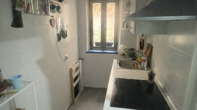 Cocina estrecha del apartamento del casco antiguo de Palma con placa de cocción, fregadero, campana extractora y ventana al patio interior.