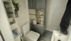 Baño compacto con inodoro, lavamanos, ducha con cortina gris y unidad de estantería en apartamento del casco antiguo de Palma.