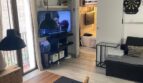 Sala de estar con mesa de comedor, sofá, televisor y vista al dormitorio, techo de vigas de madera, encanto de edificio antiguo
