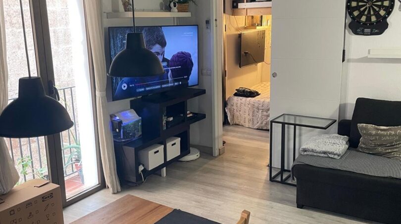 Sala de estar con mesa de comedor, sofá, televisor y vista al dormitorio, techo de vigas de madera, encanto de edificio antiguo