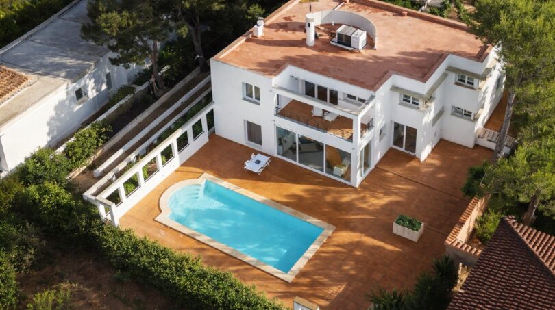 Luftaufnahme einer weißen Luxusvilla mit Pool und Terrasse in Llucmajor, umgeben von Grünflächen.