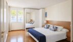 Helles Schlafzimmer der First-Line-Villa in Llucmajor mit Doppelbett, Holzboden und Meerblick durchs Fenster.