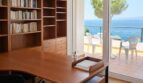 Helles Arbeitszimmer mit Holzschreibtisch, Bücherregal und Glastür zur Meerblick-Terrasse der First-Line-Villa in Llucmajor.