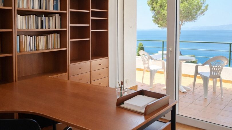 Helles Arbeitszimmer mit Holzschreibtisch, Bücherregal und Glastür zur Meerblick-Terrasse der First-Line-Villa in Llucmajor.