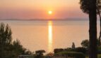 Sonnenuntergang über dem Meer mit mediterranem Garten, Skulptur und Pinien – traumhafter Meerblick der First-Line-Villa.
