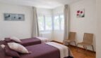 Helles Schlafzimmer der First-Line-Villa in Llucmajor mit zwei Einzelbetten, Holzboden und großen Fenstern.