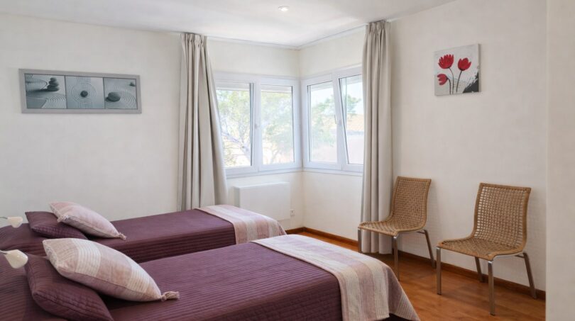 Helles Schlafzimmer der First-Line-Villa in Llucmajor mit zwei Einzelbetten, Holzboden und großen Fenstern.