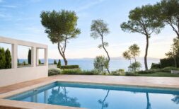 Außenpool der First-Line-Villa in Llucmajor mit direktem Meerblick, mediterranen Pinien und weißer Pergola.