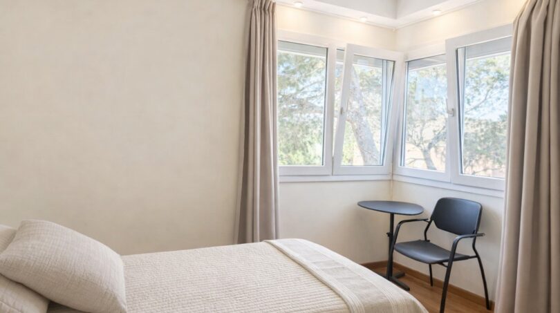 Helles Schlafzimmer der First-Line-Villa in Llucmajor mit Doppelbett, Schreibtisch und großen Fenstern zum Garten.