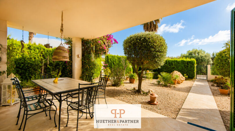 Überdachte Terrasse mit Esstisch, gepflegtem Garten und mediteraner Bepflanzung des Luxus-Chalets in Cala Murada.