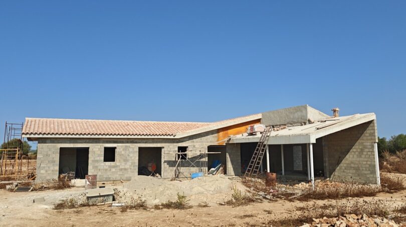 Estructura en bruto de una finca moderna en Vilafranca de Bonany con muros de piedra natural y techo de tejas mediterráneo en construcción.