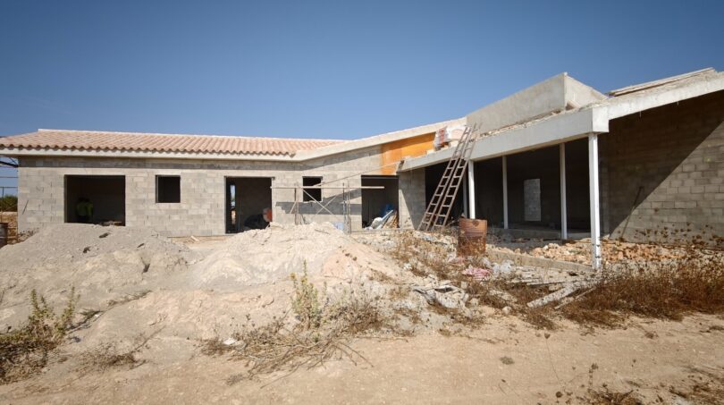 Estructura en bruto de una finca moderna en Vilafranca de Bonany con muros de hormigón, techo plano y andamios bajo cielo azul.