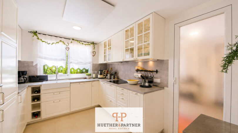 Helle Einbauküche mit weißen Fronten, Granitarbeitsflächen und Glasvitrinenschränken im Luxus-Chalet Cala Murada