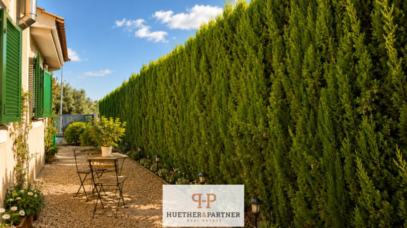 Seitlicher Gartenbereich des Luxus-Chalets in Cala Murada mit hoher Thuja-Hecke, Kiesweg und Bistrotisch.