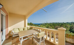 Sonnige Terrasse des Reihenhauses in Cales de Mallorca mit Sitzecke, Holztisch und Meerblick über grüne Pinien.