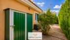 Gartenbereich des Luxus-Chalets in Cala Murada mit grünem Metallschuppen, blühendem Strauch und Zypressenhecke.