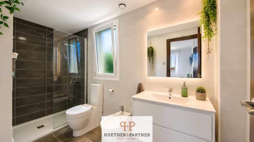 Modernes Badezimmer im Luxus-Chalet Cala Murada mit Dusche, Doppelwaschtisch, Bidet und Grünpflanzen.