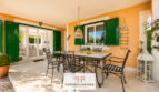 Überdachte Terrasse mit Esstisch aus Schmiedeeisen, grünen Fensterläden und mediterranem Flair im Luxus-Chalet Cala Murada