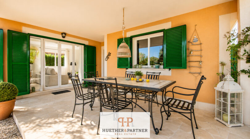 Überdachte Terrasse mit Esstisch aus Schmiedeeisen, grünen Fensterläden und mediterranem Flair im Luxus-Chalet Cala Murada