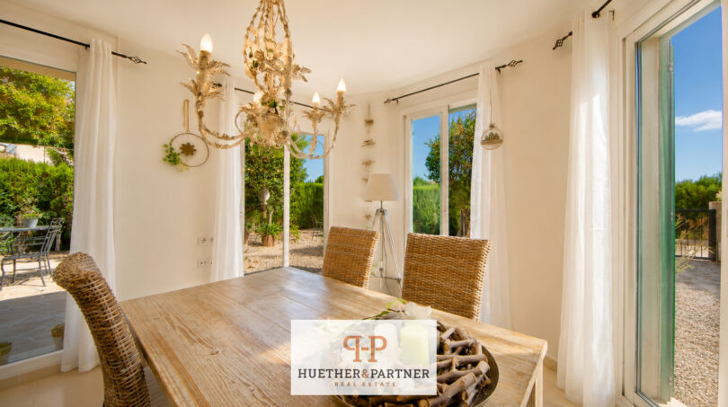 Heller Essbereich mit Holztisch, Korbstühlen und Kronleuchter, großzügige Fenster mit Gartenblick im Luxus-Chalet Cala Murada