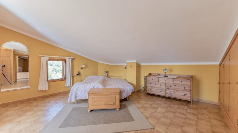 Geräumiges Schlafzimmer der Finca in Campanet mit Holzmöbeln, gelben Wänden und Terrakottaboden.